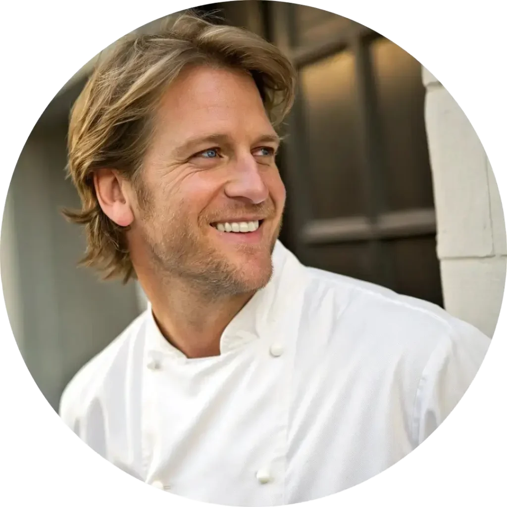 About Us 2 Smiling male chef in a white uniform standing outside a restaurant.